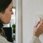 Main tournant un thermostat blanc sur un mur